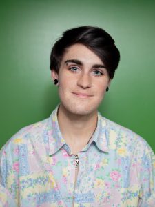 Image of person, Kai Schweizer in a floral shirt with a green background, smiling at the camera