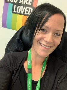 Image of woman, Wendy Caspar, in blask top smiling at camera with a rainbow pride poster in the background